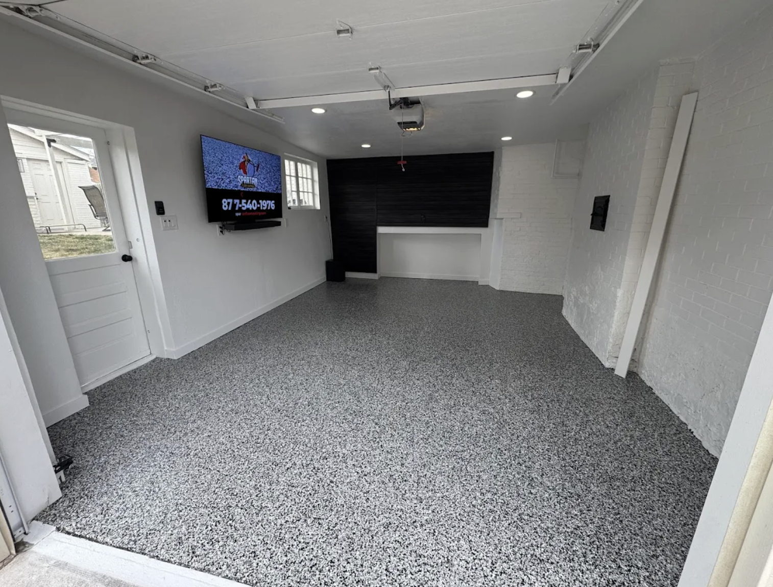 Refinished garage with decorative flake coating, television wall, and bright white trim